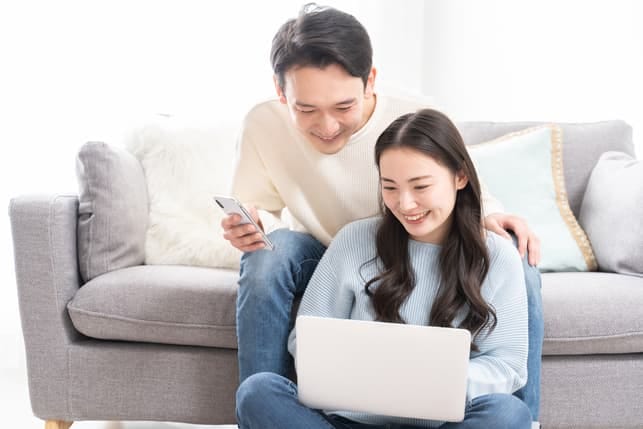 a happy Asian couple is using their gadgets together