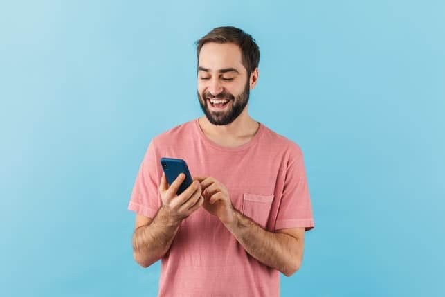 a happy man in a pink t-shirt is using his smartphone