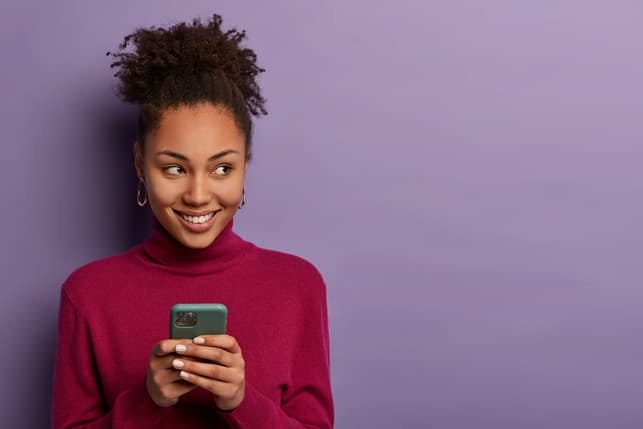 a young black woman is using her smartphone while smiling