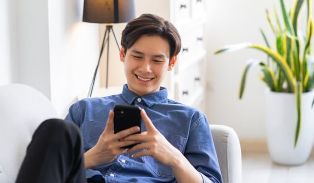 a young asian guy checking his phone while relaxing at home