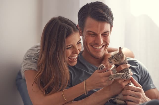 a young couple is playing with a kitten together at home